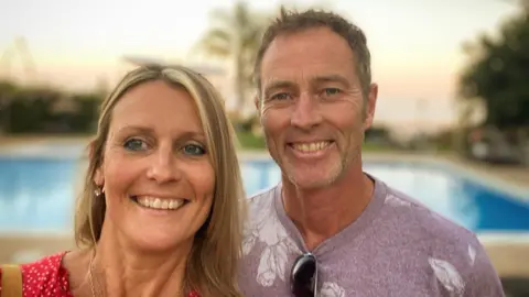 Family handout Lindsay Foreman and Craig Foreman smile as they pose together for a selfie picture. Behind them is a swimming pool. She is wearing a red top and him a lilac T-shirt.